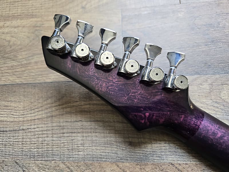 Pink and black guitar headstock with tuning pegs on a wooden surface