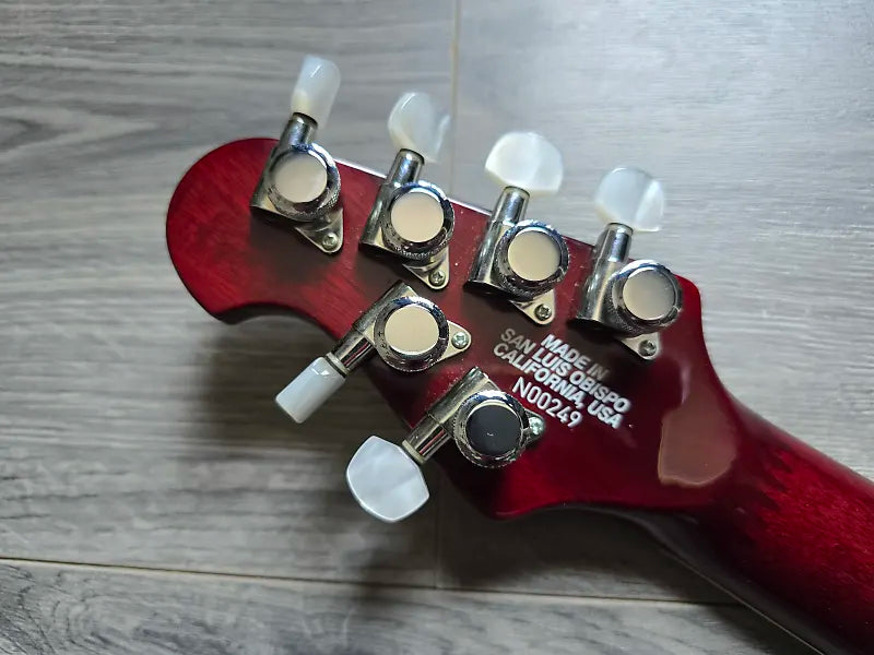 Maroon guitar headstock with tuning pegs on a wooden surface