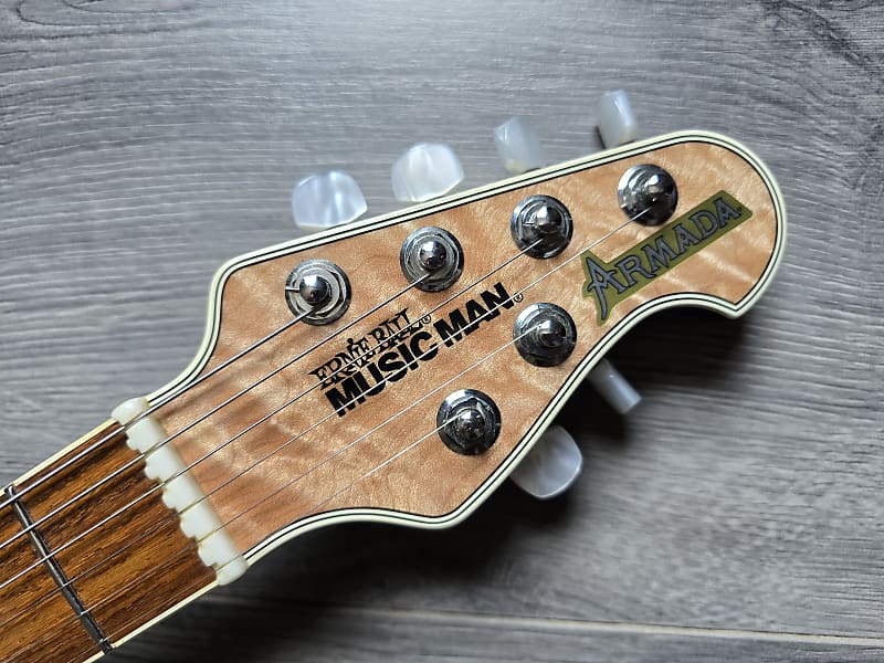 Guitar headstock with 'Ernie Ball Music Man' branding on a wooden surface
