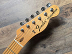 Fender Telecaster guitar headstock showing logo and tuning pegs on a wooden surface