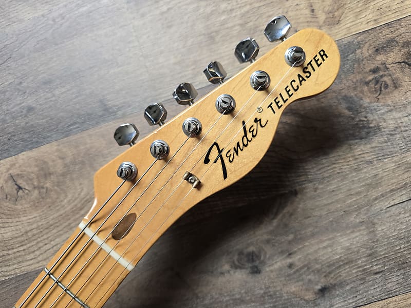 Fender Telecaster guitar headstock showing logo and tuning pegs on a wooden surface
