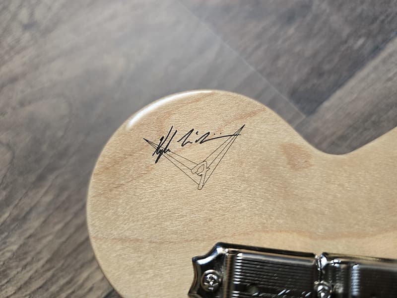 Close-up of a guitar's wooden headstock with a signature on a wooden surface