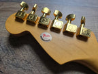 Gold guitar tuners on a wooden guitar body with Fender logo.