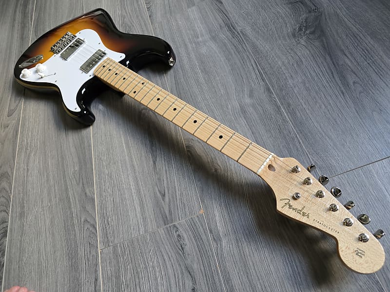 Fender Stratocaster with a maple neck and fretboard lying on a wooden surface.