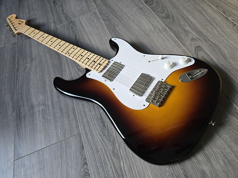 Electric guitar with a sunburst finish and white pickguard on a wooden floor