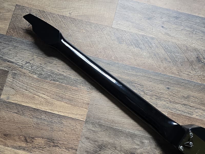 back of a black electric guitar neck lying on a wooden surface