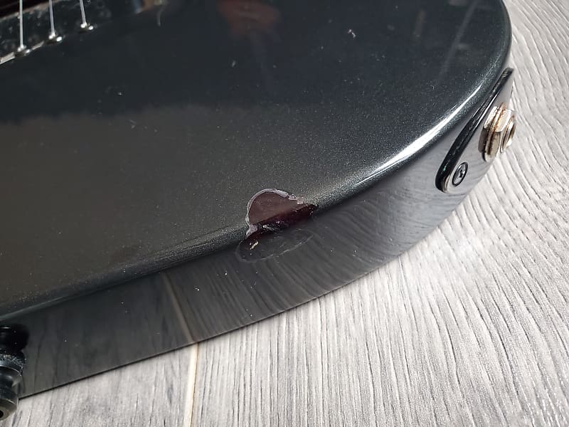 Close-up of a black electric guitar with a small chip in the paint