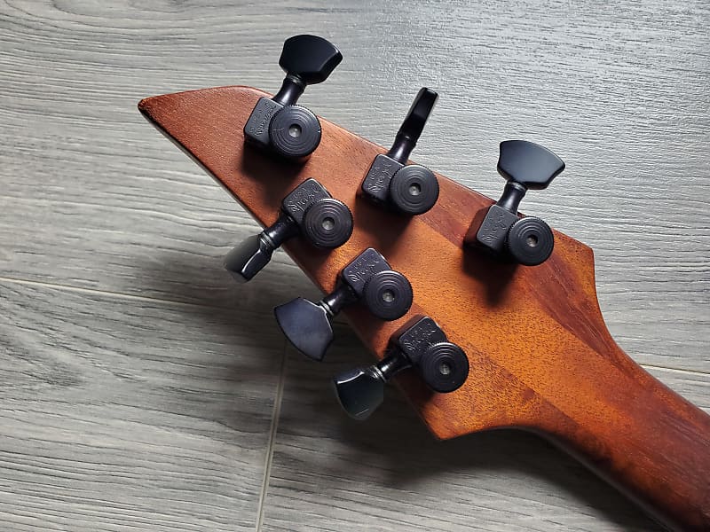 Close-up of a wooden guitar headstock with tuning pegs on a wooden surface