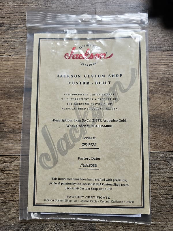 Jackson Custom Shop certificate in clear plastic packaging on a wooden surface