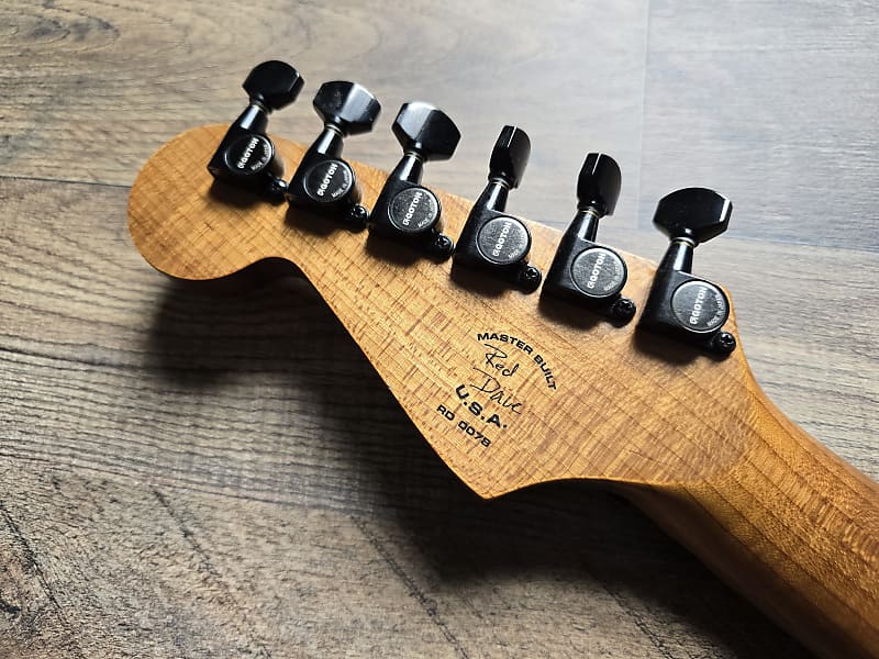 Wooden guitar headstock with black tuning pegs on a wooden surface