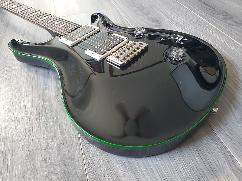 Black electric guitar with gloss finish and green accent on a wooden floor