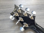 Close-up of a guitar headstock with tuning pegs on a wooden surface