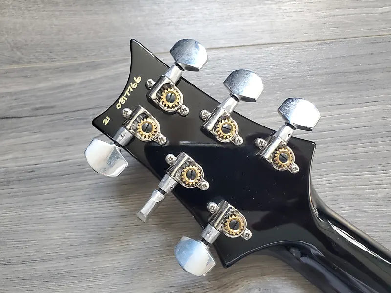 Close-up of a guitar headstock with tuning pegs on a wooden surface