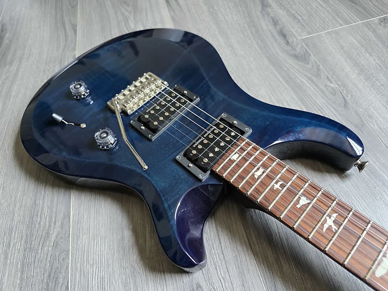 Blue electric guitar with a rosewood fretboard lying on a wooden floor