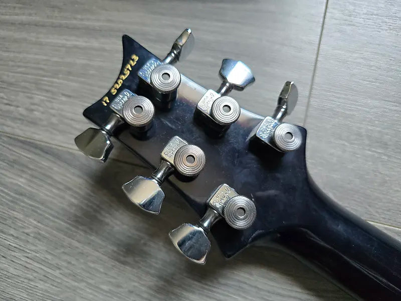 Guitar headstock with tuning pegs on a wooden surface