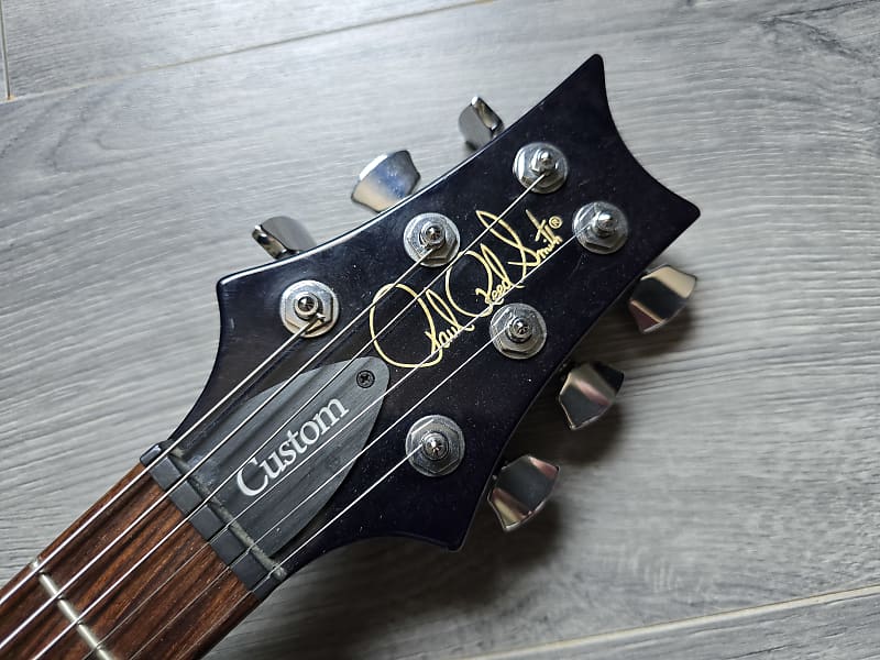 Guitar headstock with 'Custom' and 'Paul Reed Smith' branding on a wooden surface