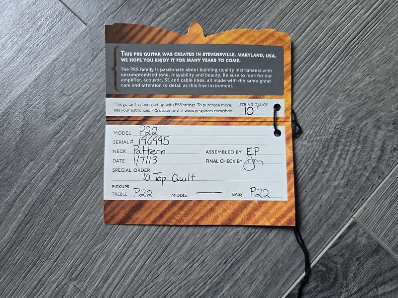 Guitar label with detailed information on a wooden stand against a gray wooden floor background