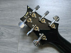 Black guitar headstock with tuning pegs on a wooden surface