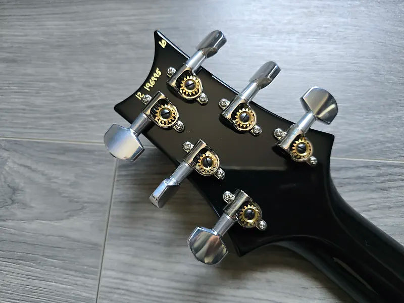 Black guitar headstock with tuning pegs on a wooden surface