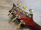 Red guitar headstock with gold tuning pegs on a wooden surface