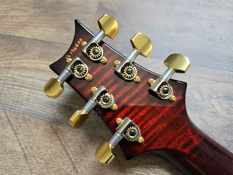 Red guitar headstock with gold tuning pegs on a wooden surface