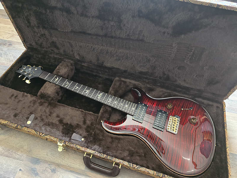 Red PRS electric guitar in a case on a wooden floor