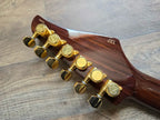 Wooden guitar headstock with gold tuning pegs on a wooden surface