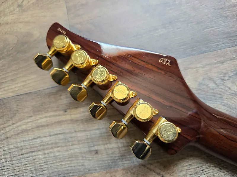 Wooden guitar headstock with gold tuning pegs on a wooden surface