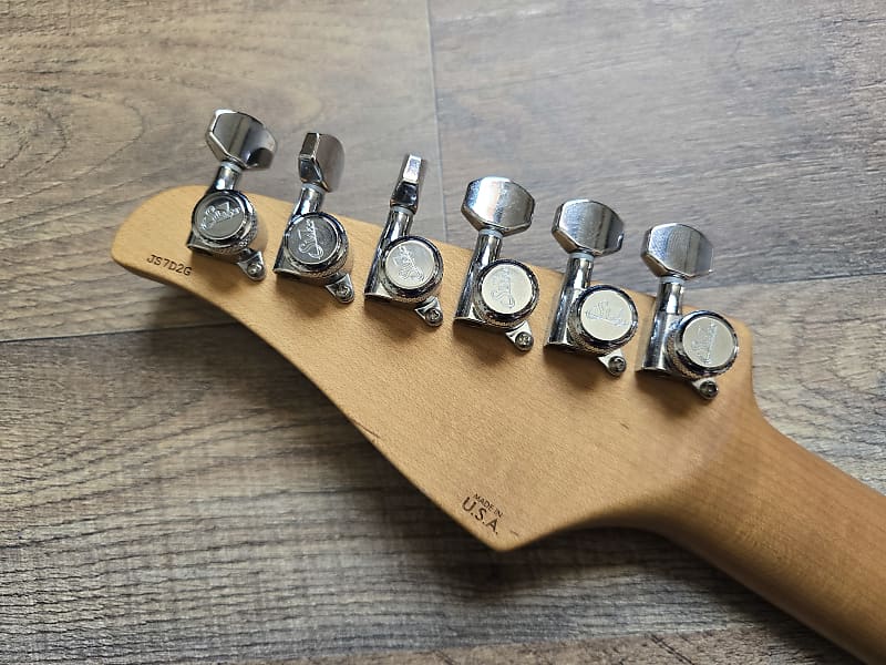 Guitar tuning pegs on a wooden neck with a serial number.