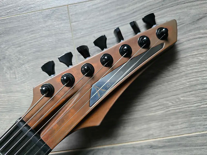Close-up of an Aristides guitar headstock with black tuning pegs
