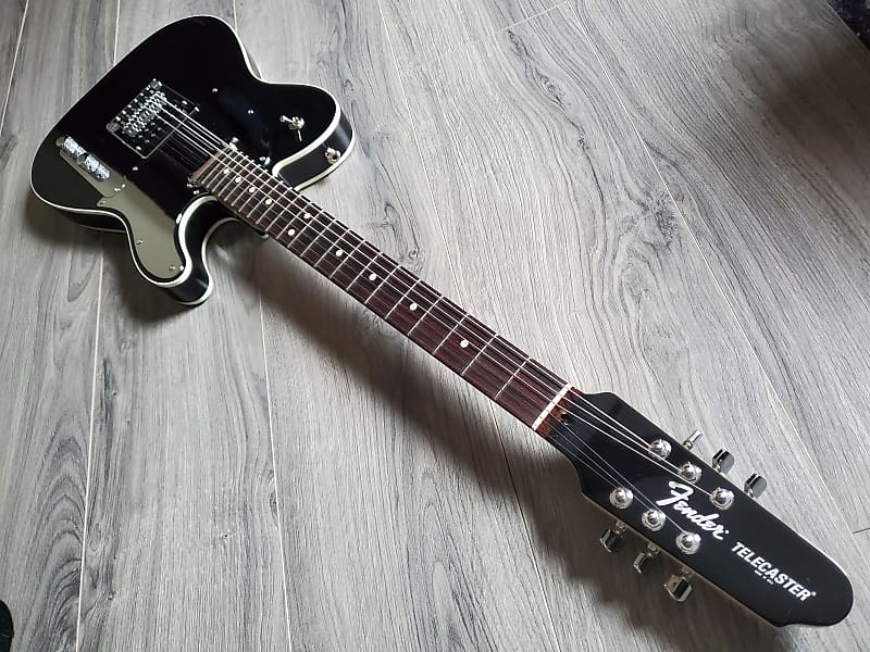 Black Fender Telecaster with a rosewood fretboard lying on a wooden surface.