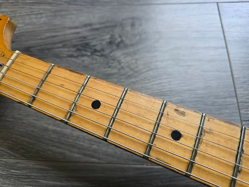 Close-up of a guitar neck with frets and strings on a wooden surface