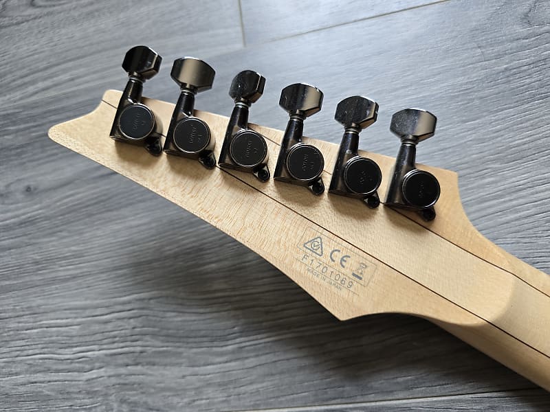 Guitar tuning pegs on a wooden neck with CE marking on a gray wooden surface
