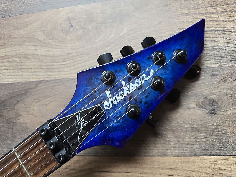 Blue electric guitar headstock with 'Jackson' branding on a wooden surface