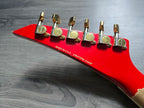 Red guitar headstock with gold tuning pegs on a wooden surface