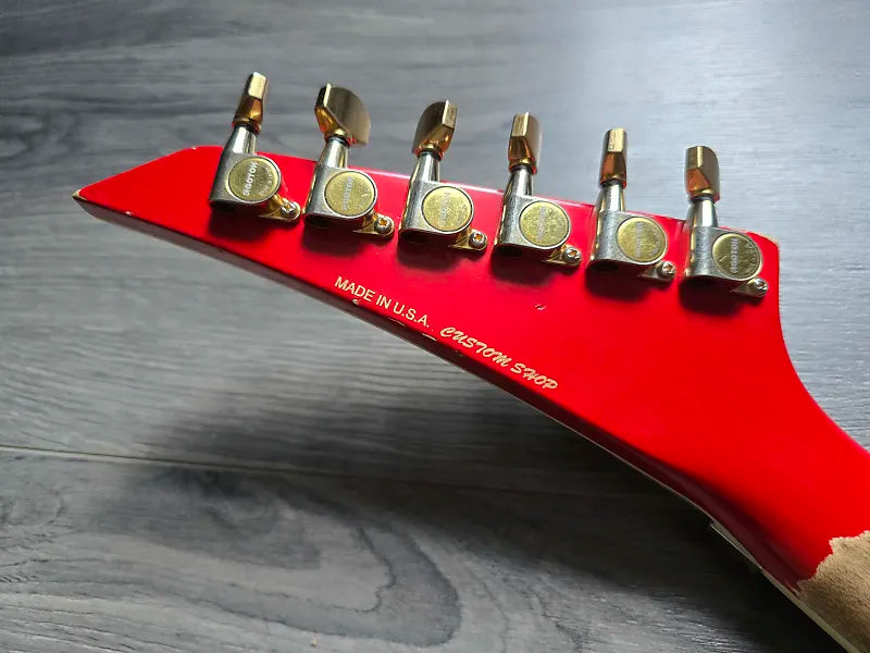 Red guitar headstock with gold tuning pegs on a wooden surface