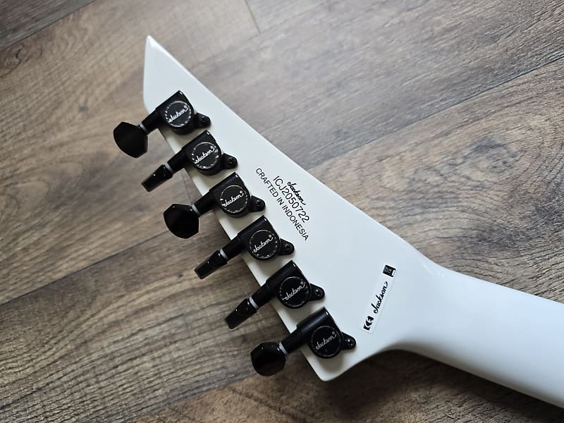 Close-up of a white electric guitar neck with black tuning pegs 