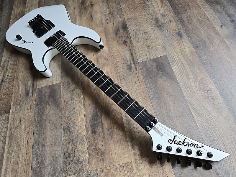 White electric guitar on a wooden floor with 'Jackson' branding, showing scale length and ebony fretboard