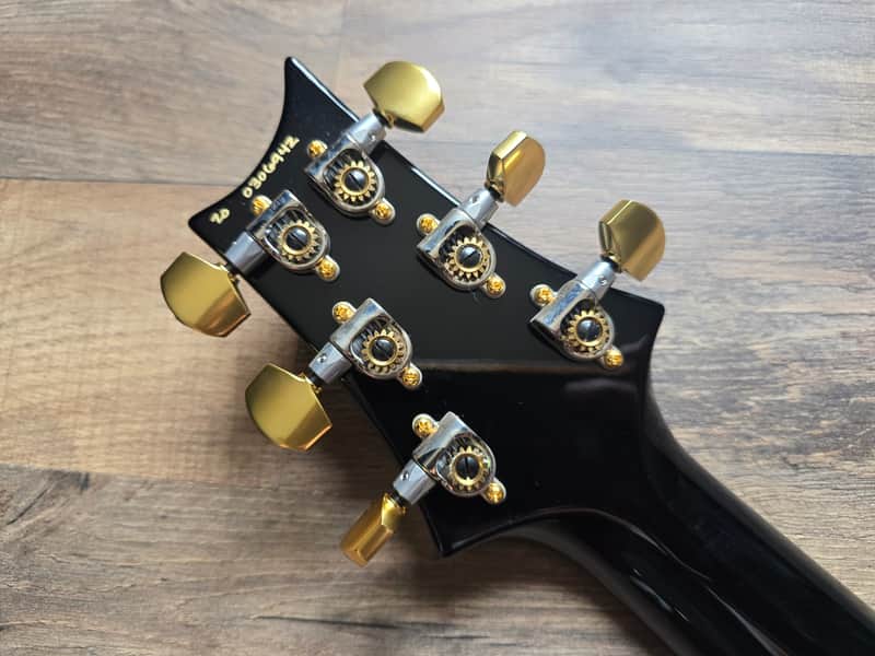 Guitar headstock with gold tuning pegs on a wooden surface