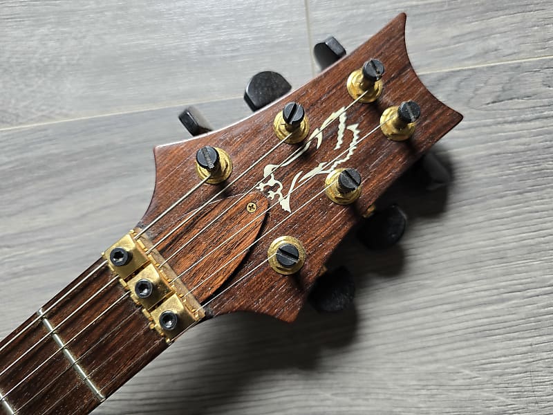 Close-up of a PRS guitar headstock with tuning pegs on a wooden surface