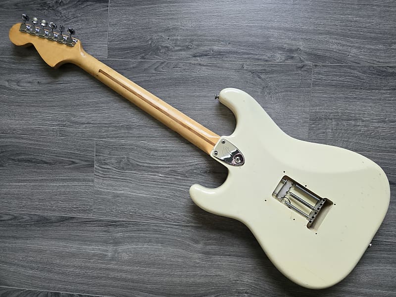 White Fender electric guitar lying face down on a gray wooden surface.